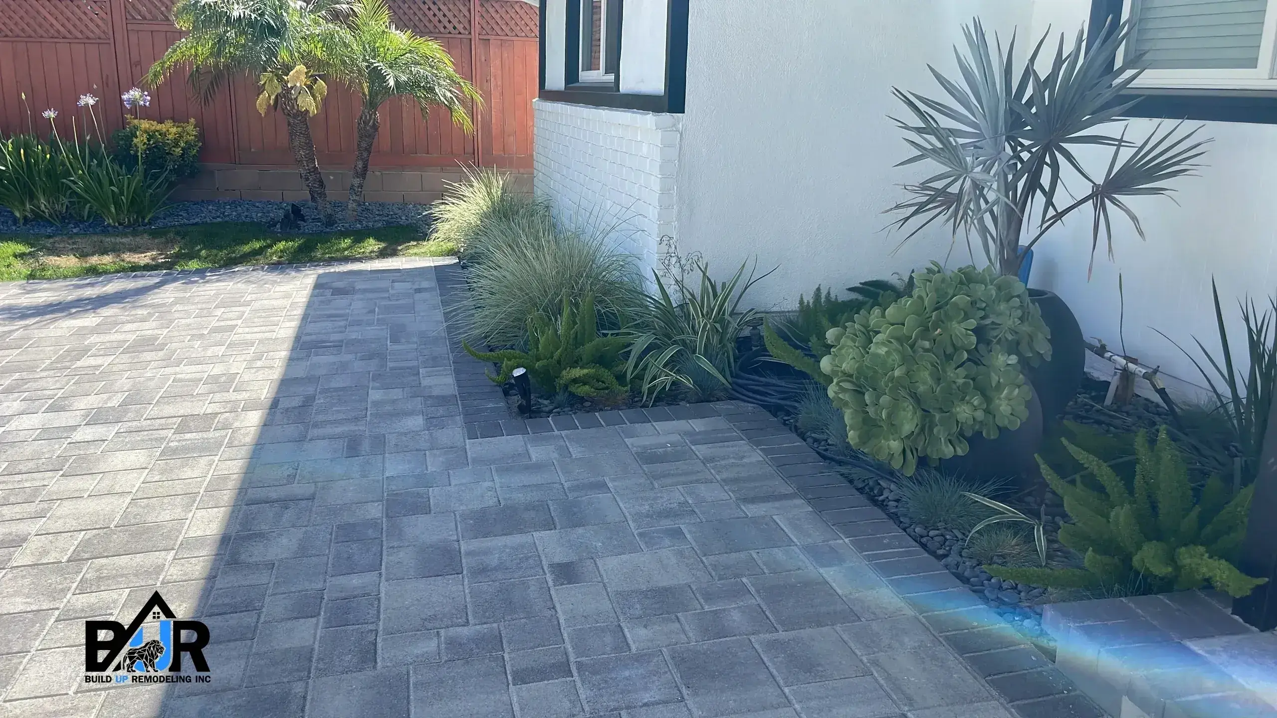 A neatly paved walkway beside a white building with various plants.