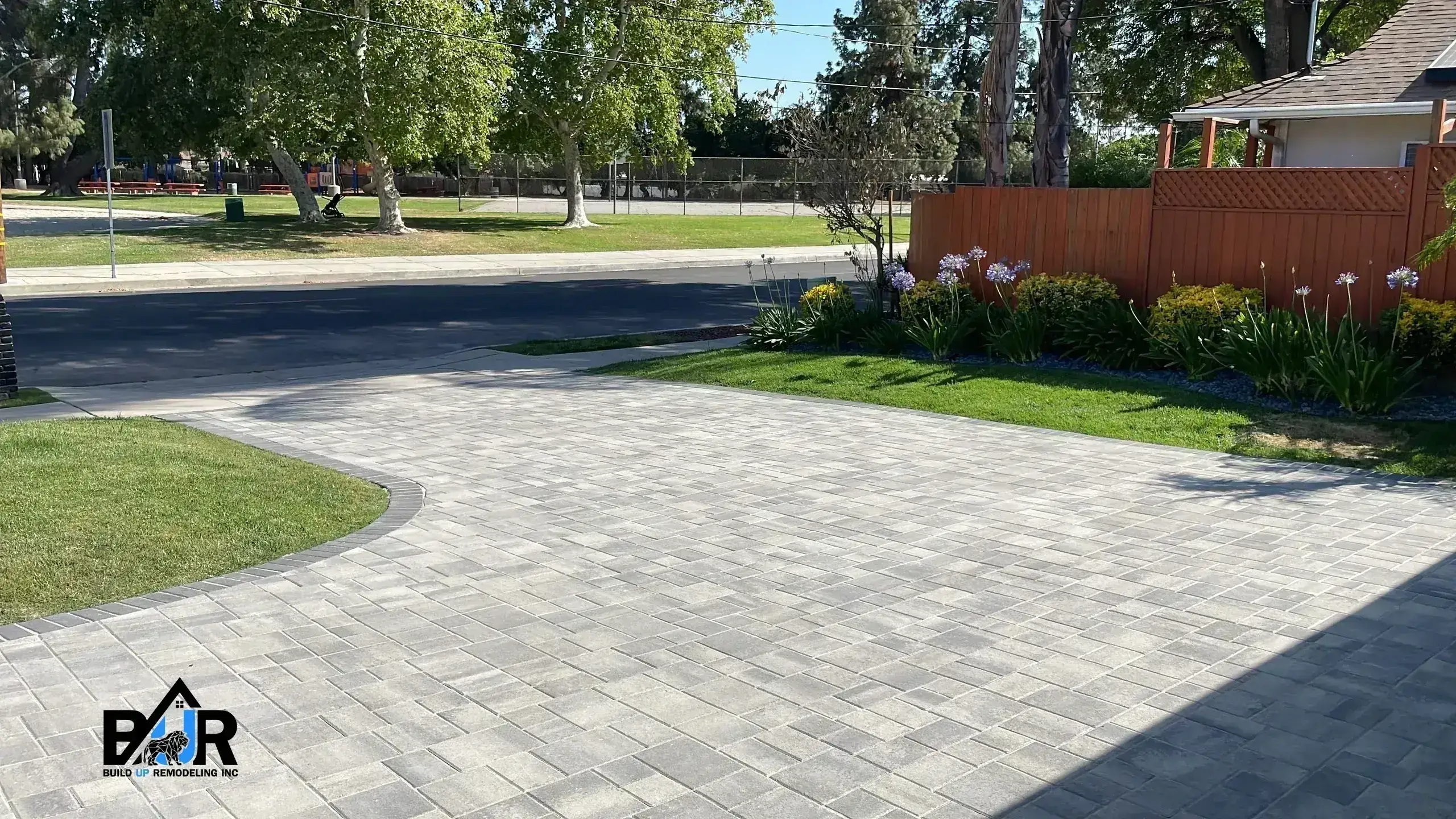 A clean, paved driveway with green grass and trees surrounding it.