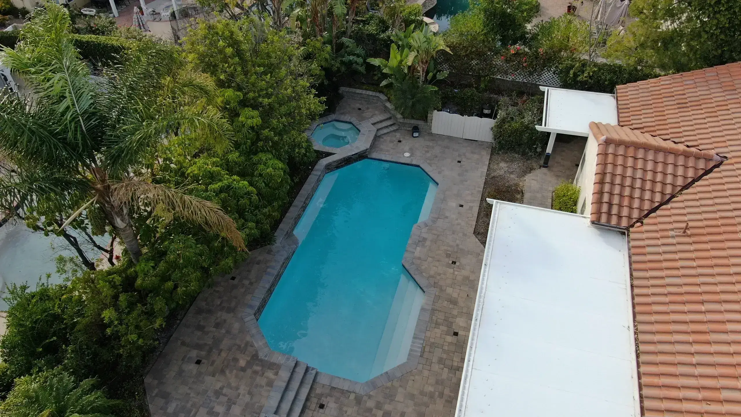 A backyard swimming pool with a hot tub and surrounding stone patio.