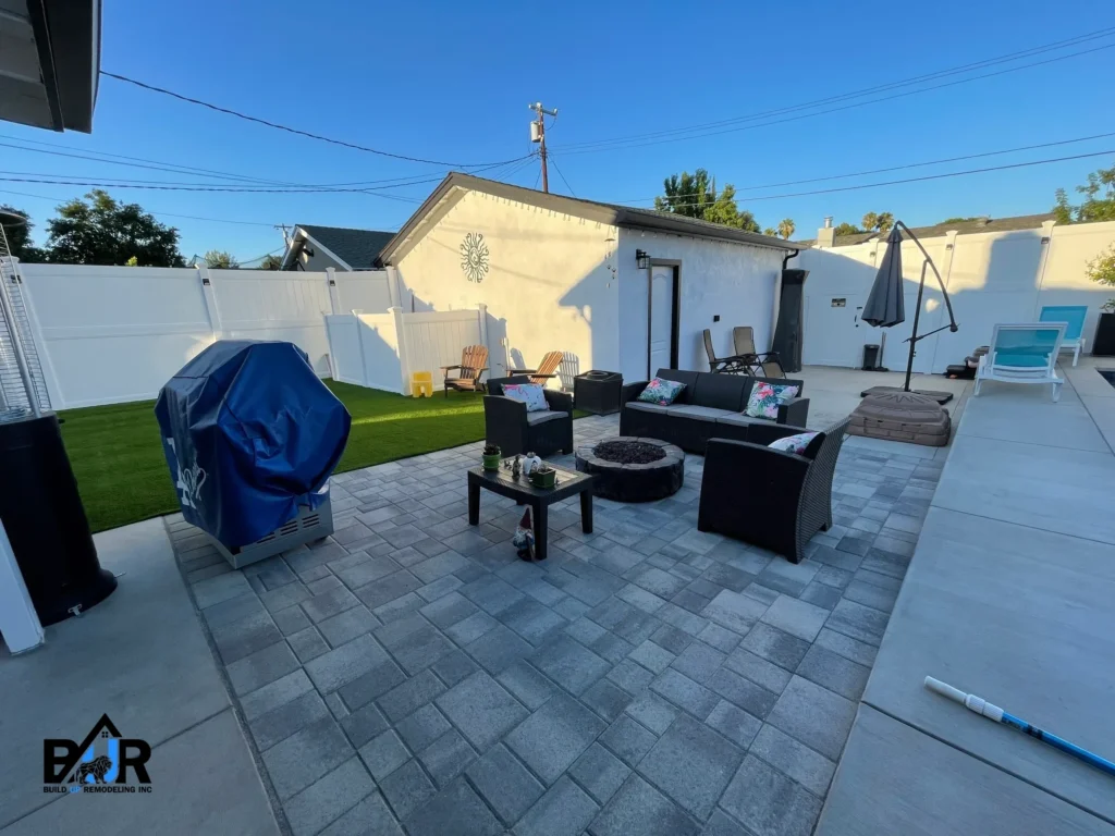 Modern backyard patio with outdoor furniture and a grill under a clear sky.