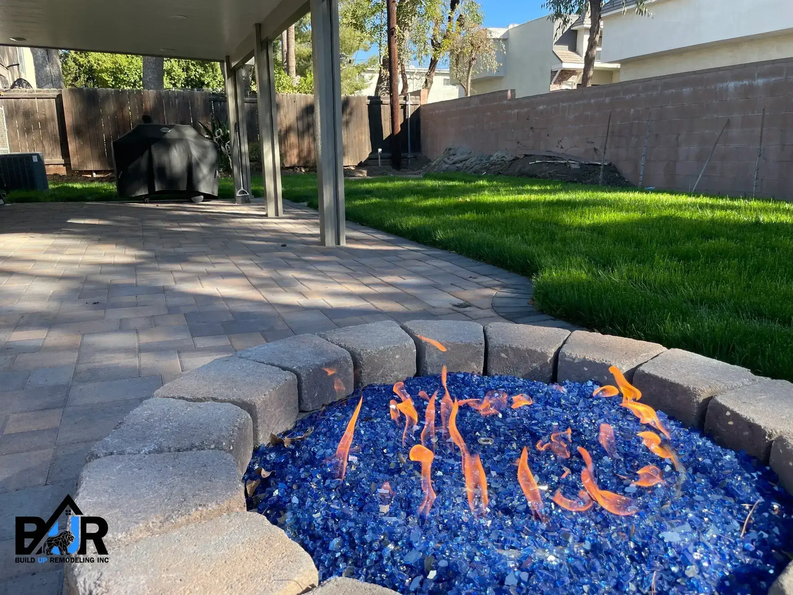 Outdoor fire pit with blue glass stones and orange flames on a patio.