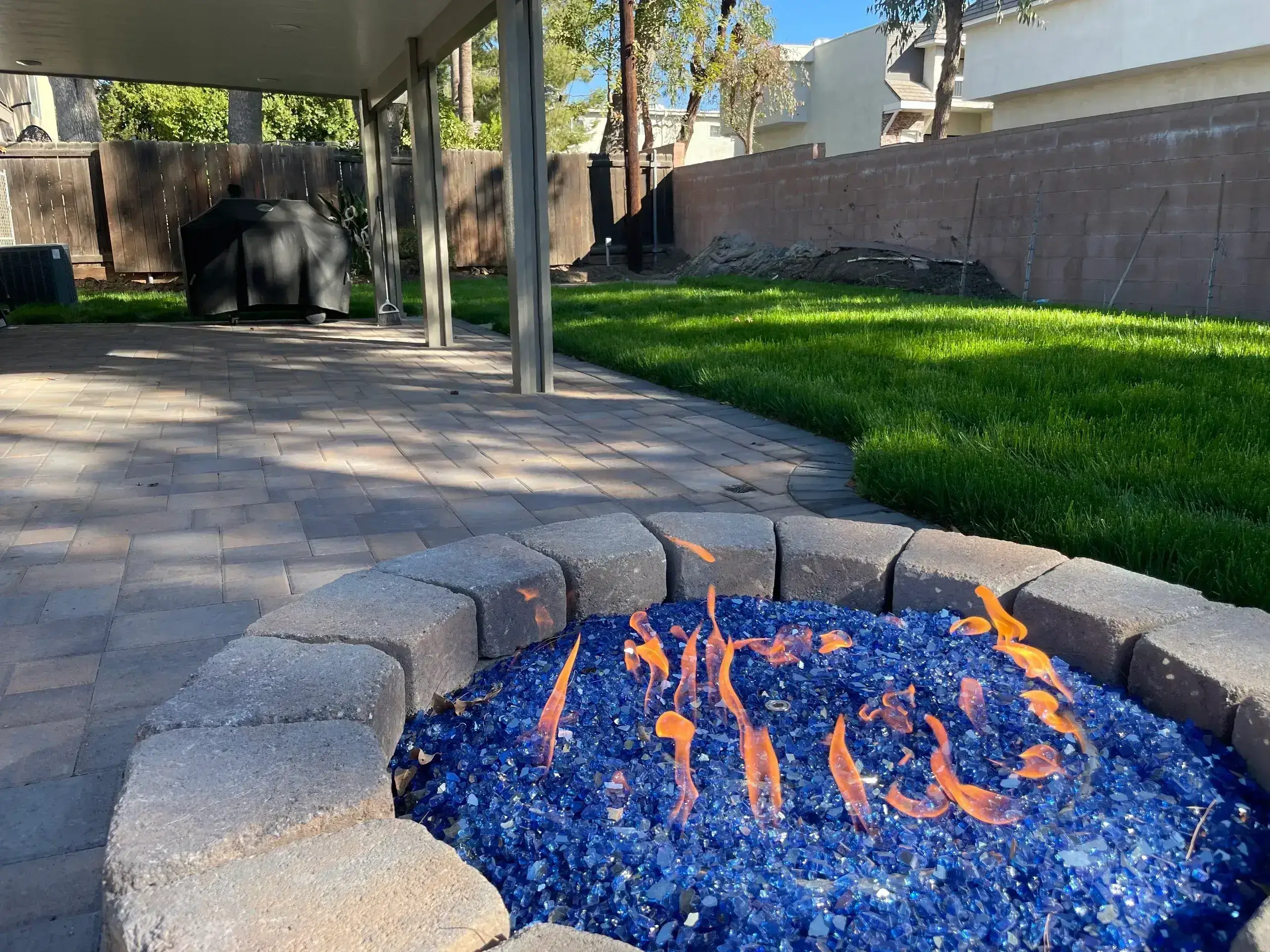Outdoor fire pit with blue glass stones and orange flames.