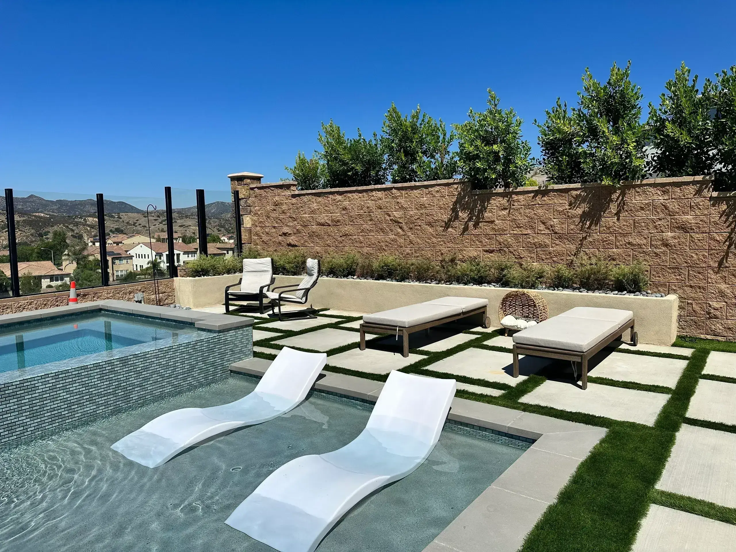 Modern backyard pool with lounge chairs and water features under clear blue sky.
