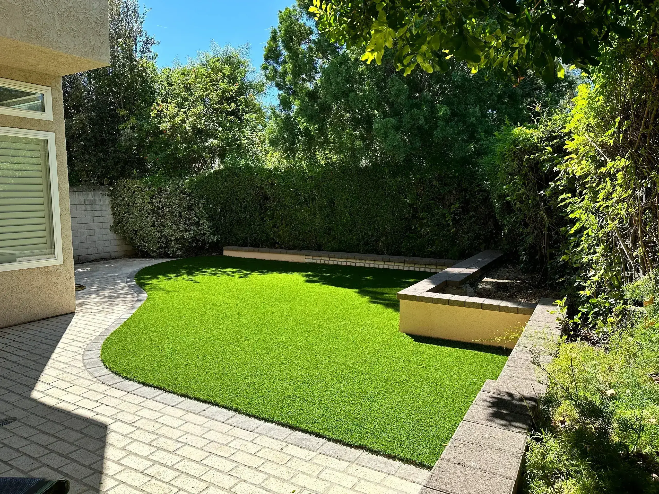 A small, well-maintained backyard with green grass and shaded seating area.