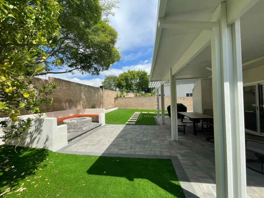 Modern backyard with artificial grass, seating area, and shaded patio space.