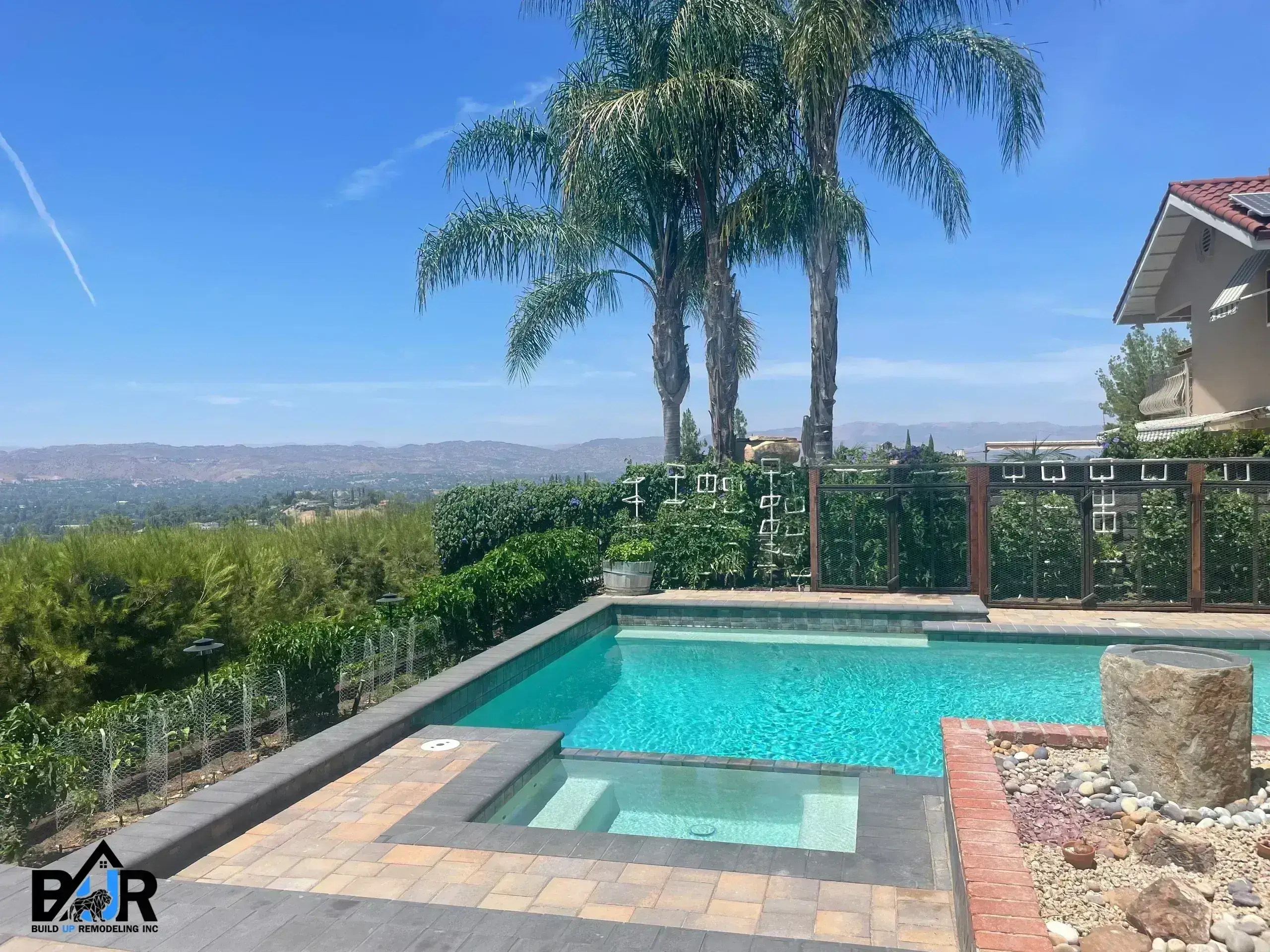 A serene backyard pool with palm trees and a distant view under a clear blue sky.