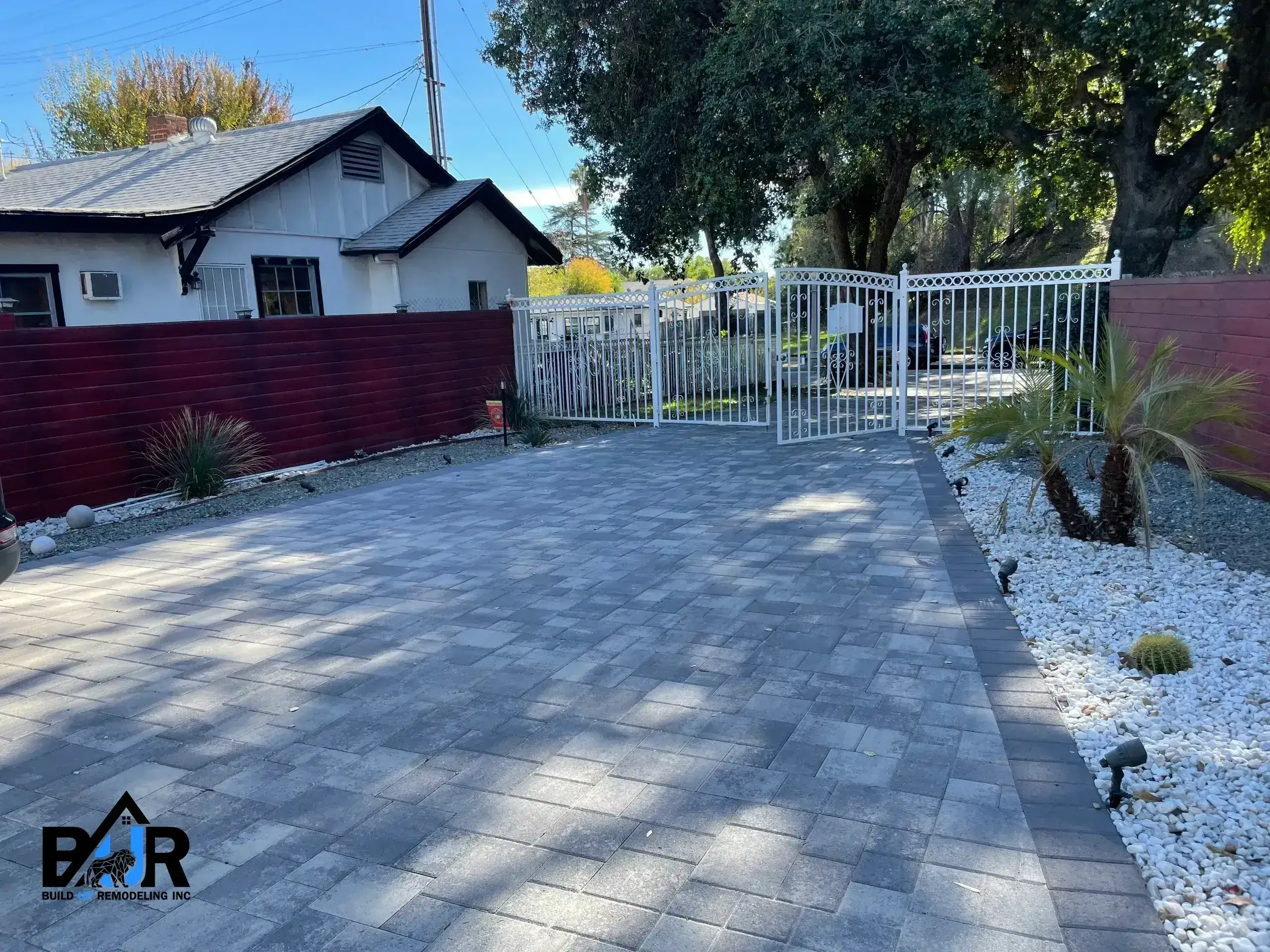 A paved driveway leading to a gated residential area with houses and trees.