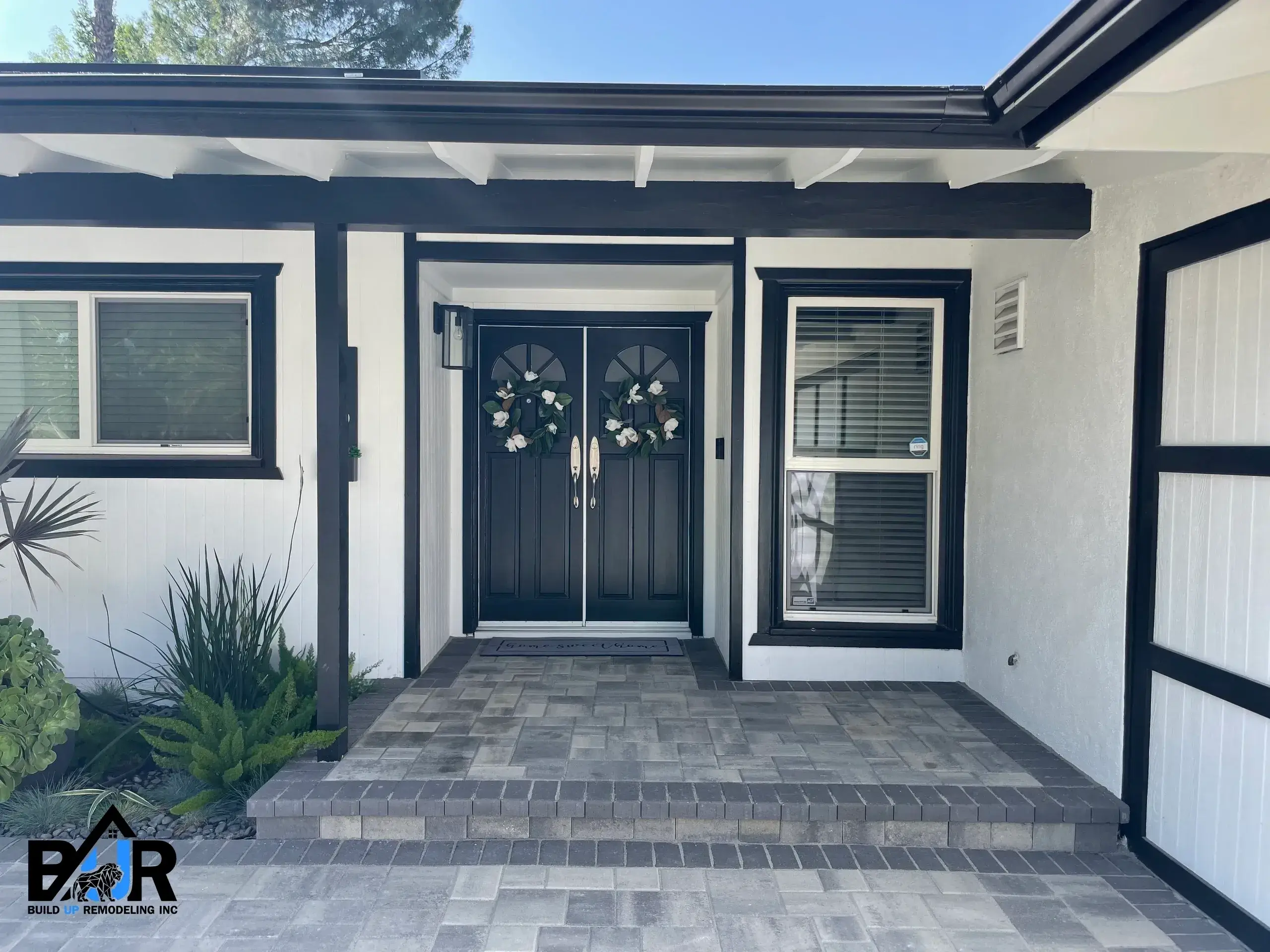 Modern house entrance with double black doors and potted plants.