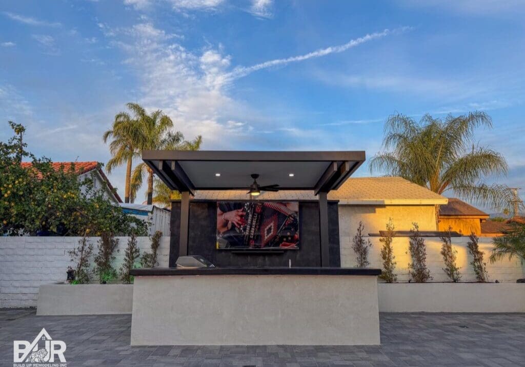 Outdoor kitchen with TV and palm trees.